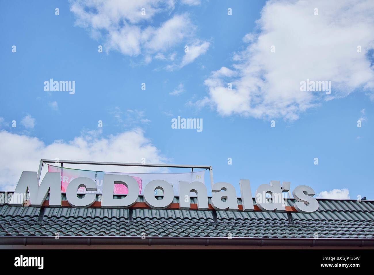 Un'inquadratura a basso angolo del logo di un fast food sotto un cielo nuvoloso blu in Germania Foto Stock