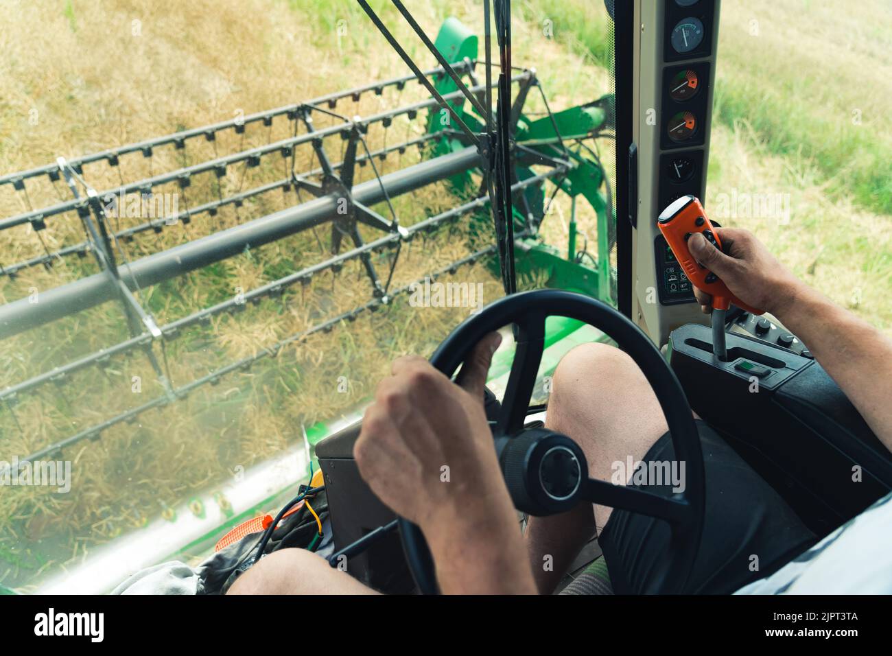 Operatore della mietitrebbia maschio caucasico non riconoscibile che guida la macchina agricola con una mano e con l'altra utilizza uno speciale telecomando. Foto di alta qualità Foto Stock