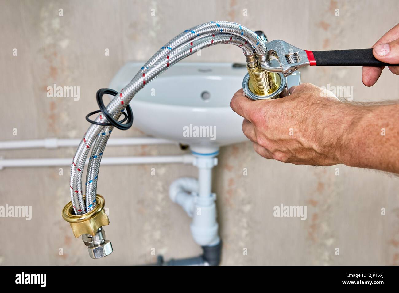 Lavori idraulici per sostituire il rubinetto dell'acqua nel bagno, l'idraulico fissa il tubo di collegamento intrecciato sul rubinetto. Foto Stock