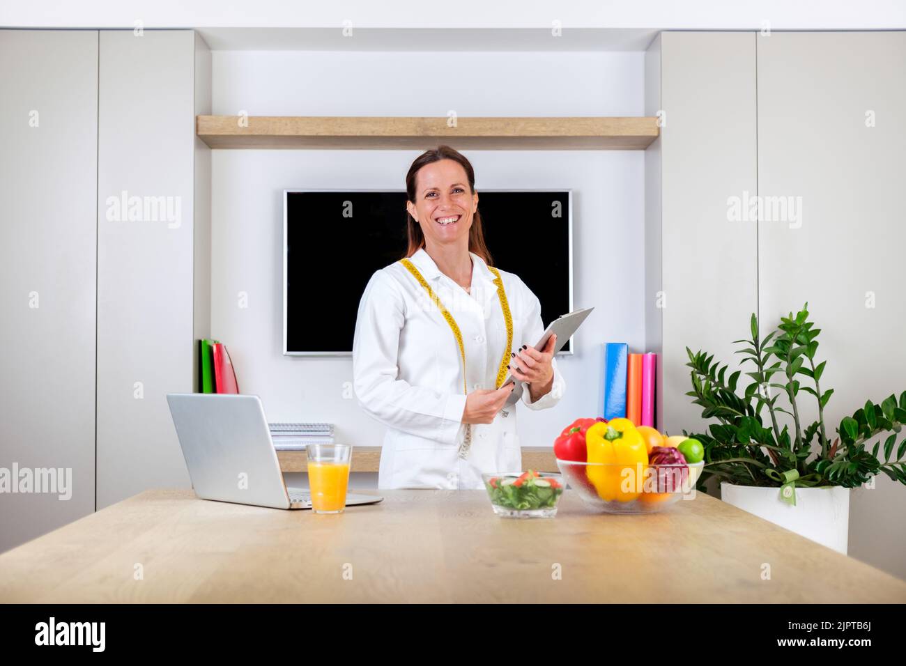 Ritratto di una giovane donna sorridente medico nutrizionista in piedi tenendo bilancia e metro a nastro in sala ufficio moderna e luminosa Foto Stock