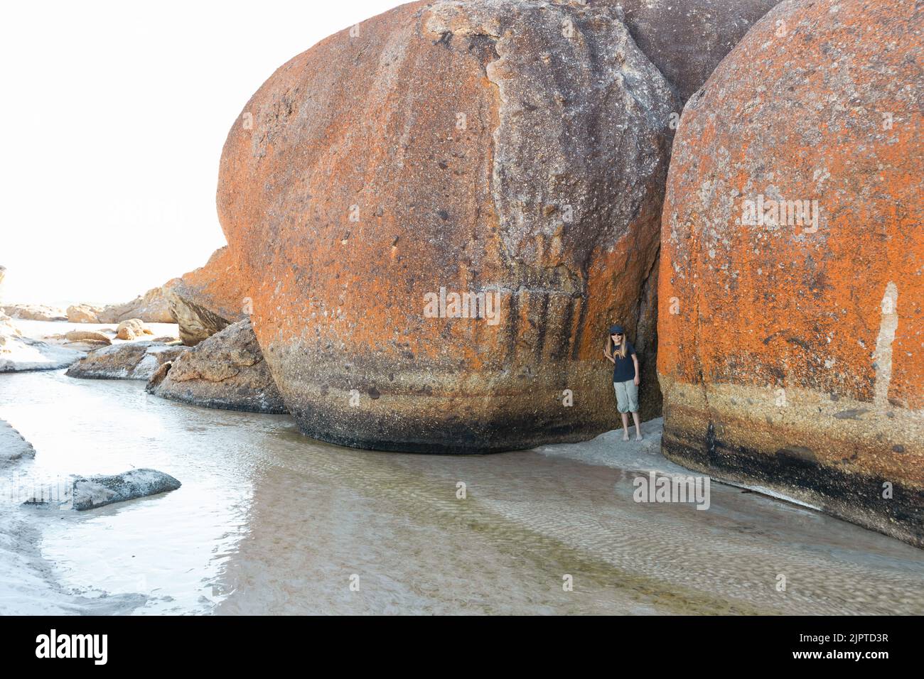 Una bambina che indossa occhiali da sole e un cappello accanto a rocce di masso sulla spiaggia Squeaky nel promontorio South Gippsland Australia di Wilson Foto Stock