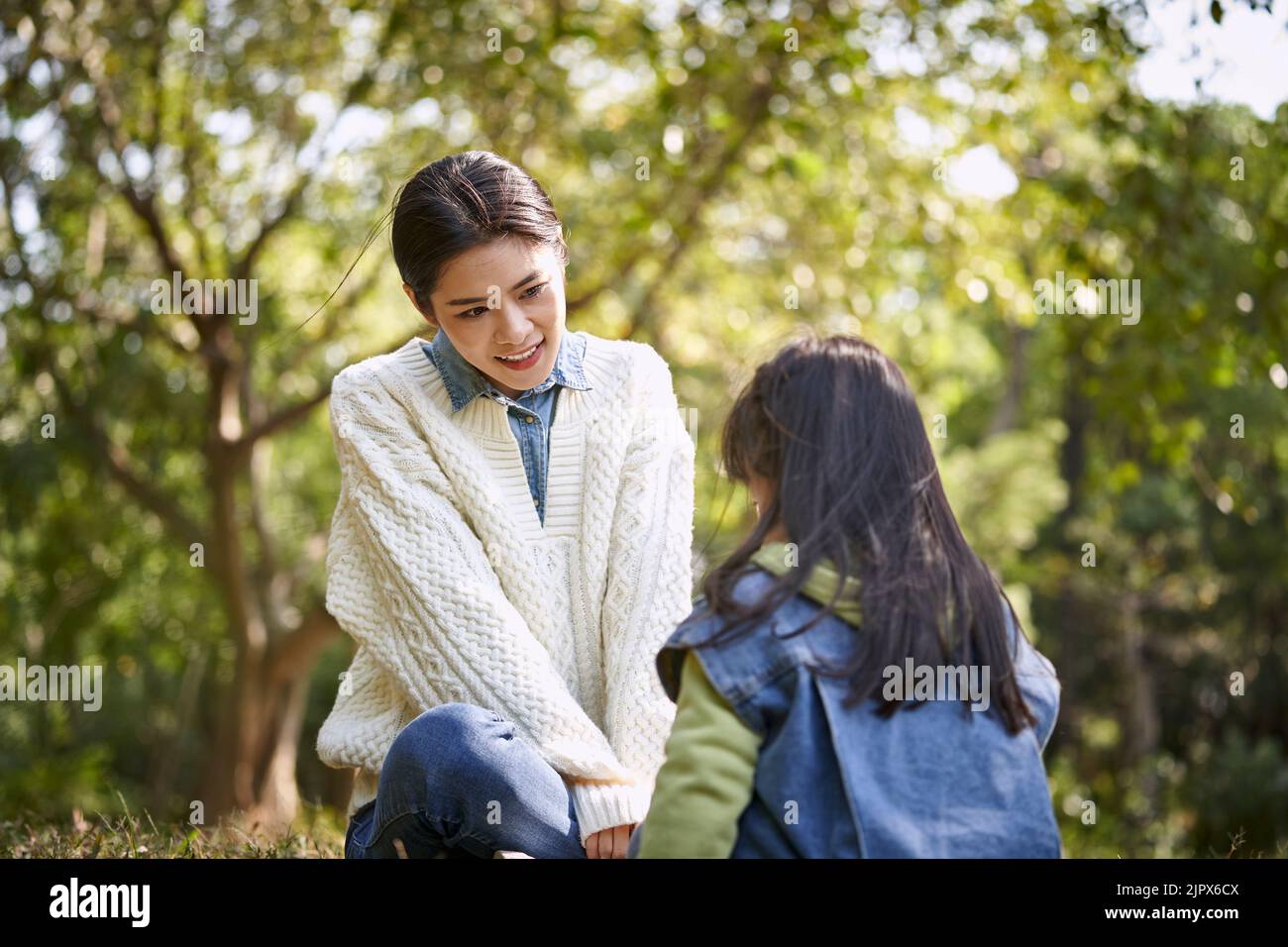 giovane madre asiatica seduta sull'erba nel parco con una piacevole conversazione con la figlia prescolare Foto Stock