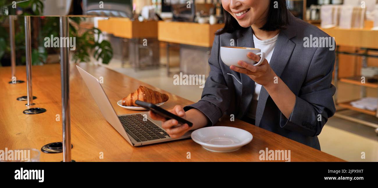 Giovane donna asiatica d'affari vestito bere caffè utilizzando il telefono nel caffè. Foto Stock