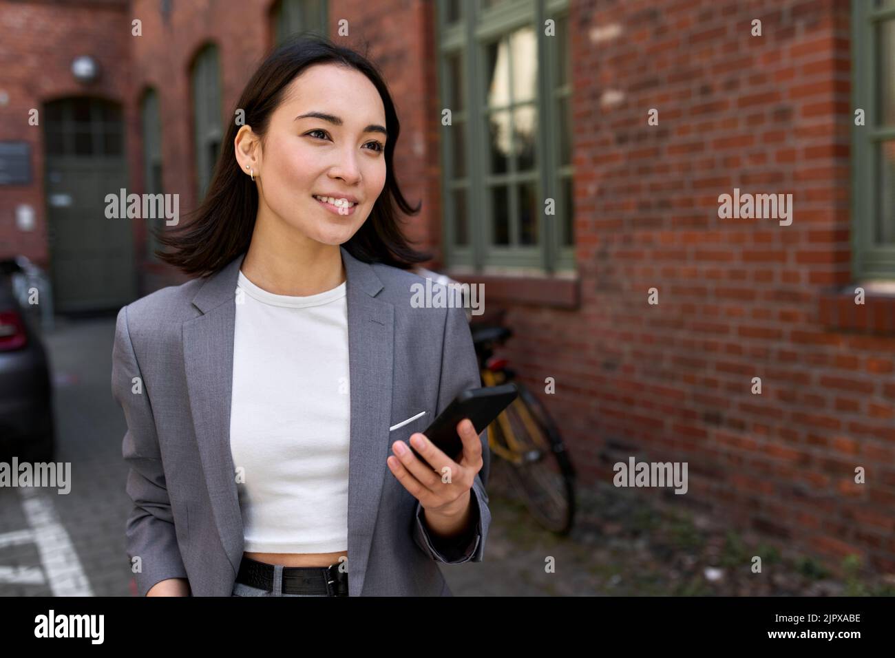 Giovane donna asiatica d'affari che indossa il vestito in piedi fuori utilizzando il telefono. Foto Stock