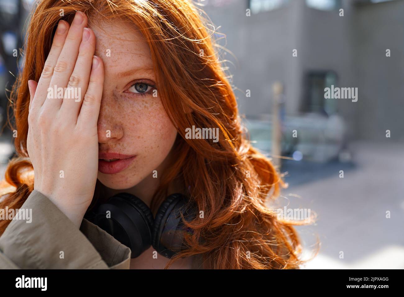 Teen redhead hipster ragazza che guarda la macchina fotografica in piedi su sfondo urbano. Foto Stock
