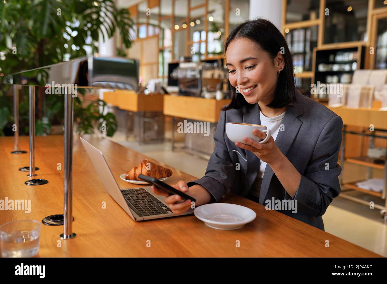 Giovane donna asiatica d'affari vestito bere caffè utilizzando il telefono nel caffè. Foto Stock