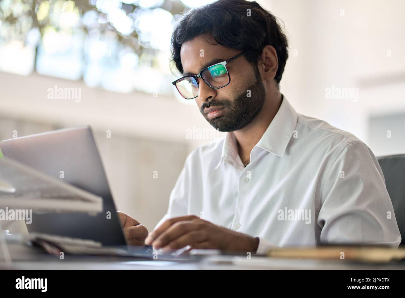 Occupato dipendente indiano che lavora a digitare sul computer portatile seduto alla scrivania. Foto Stock