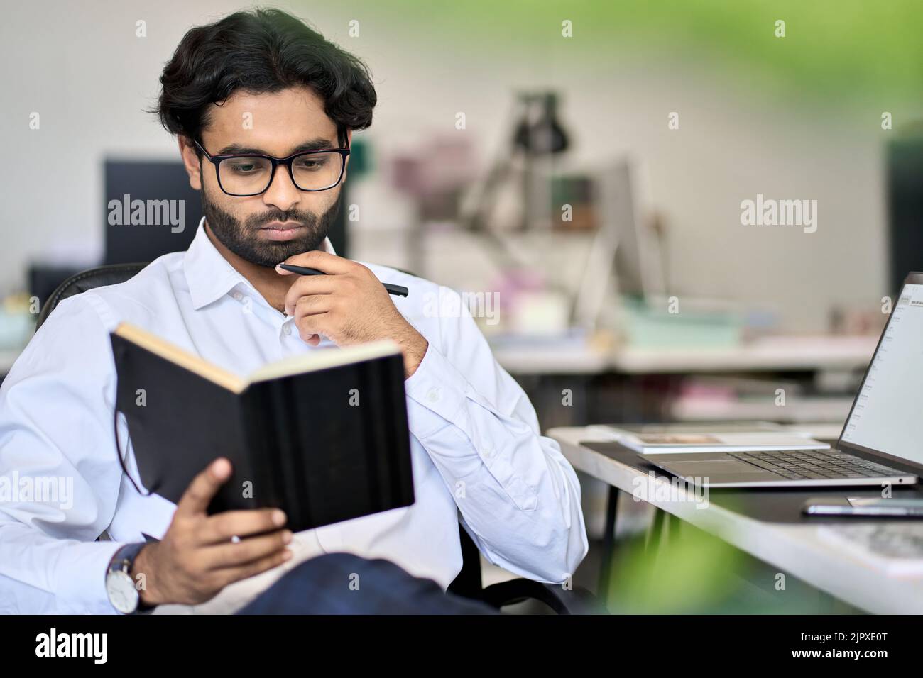 Agenda di pianificazione dipendente maschile indiano occupato nel notebook che lavora in ufficio. Foto Stock