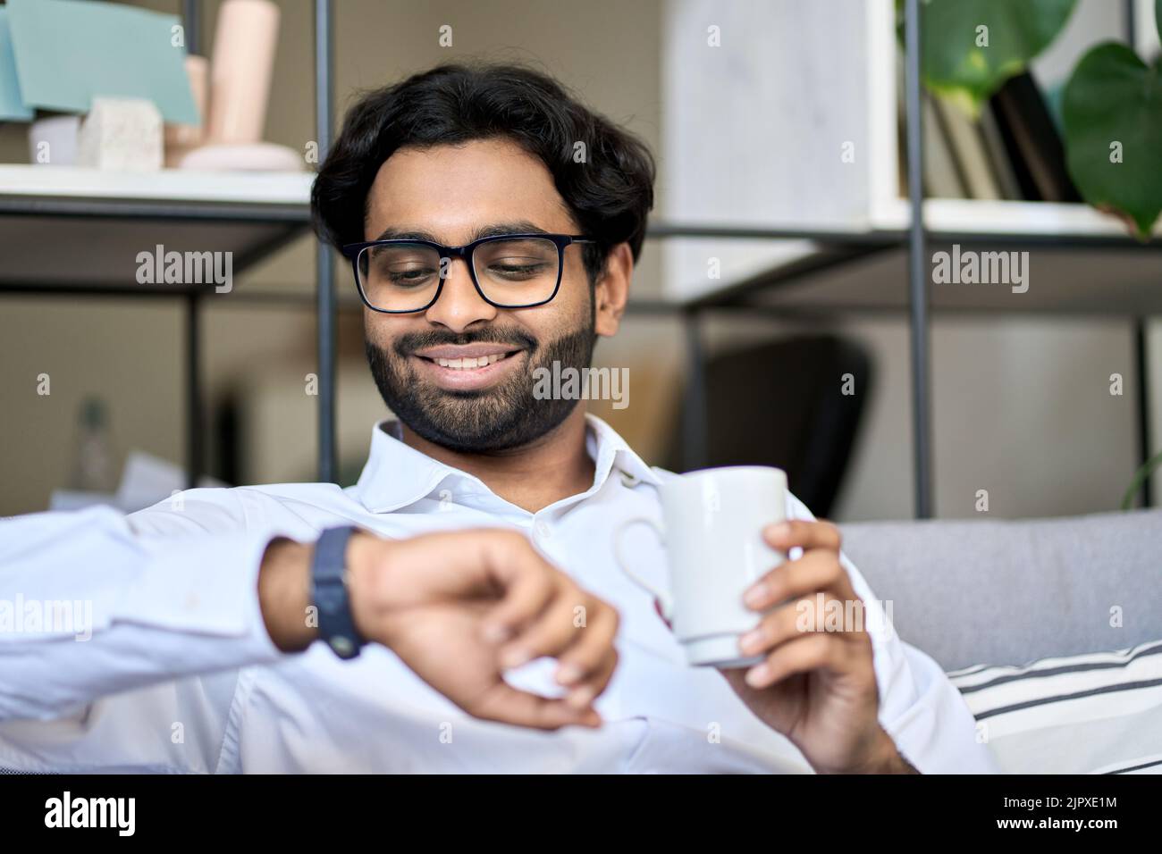 Uomo d'affari indiano sorridente che beve caffè la mattina che controlla l'orario. Foto Stock