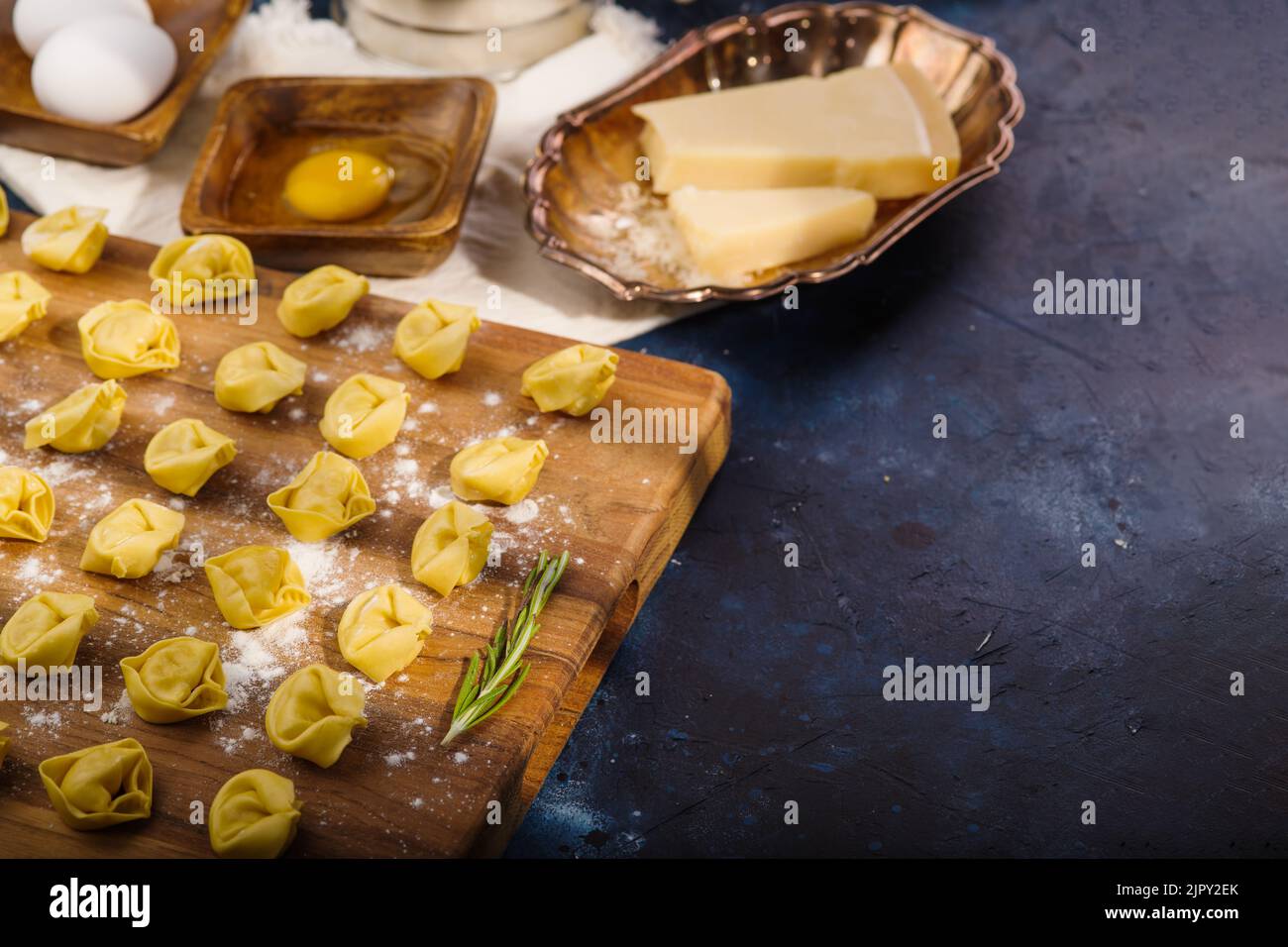 Piccoli gnocchi crudi, ravioli su un tagliere di legno su sfondo blu scuro. Processo di cottura. Ingredienti, utensili da cucina. Non ci sono persone Foto Stock