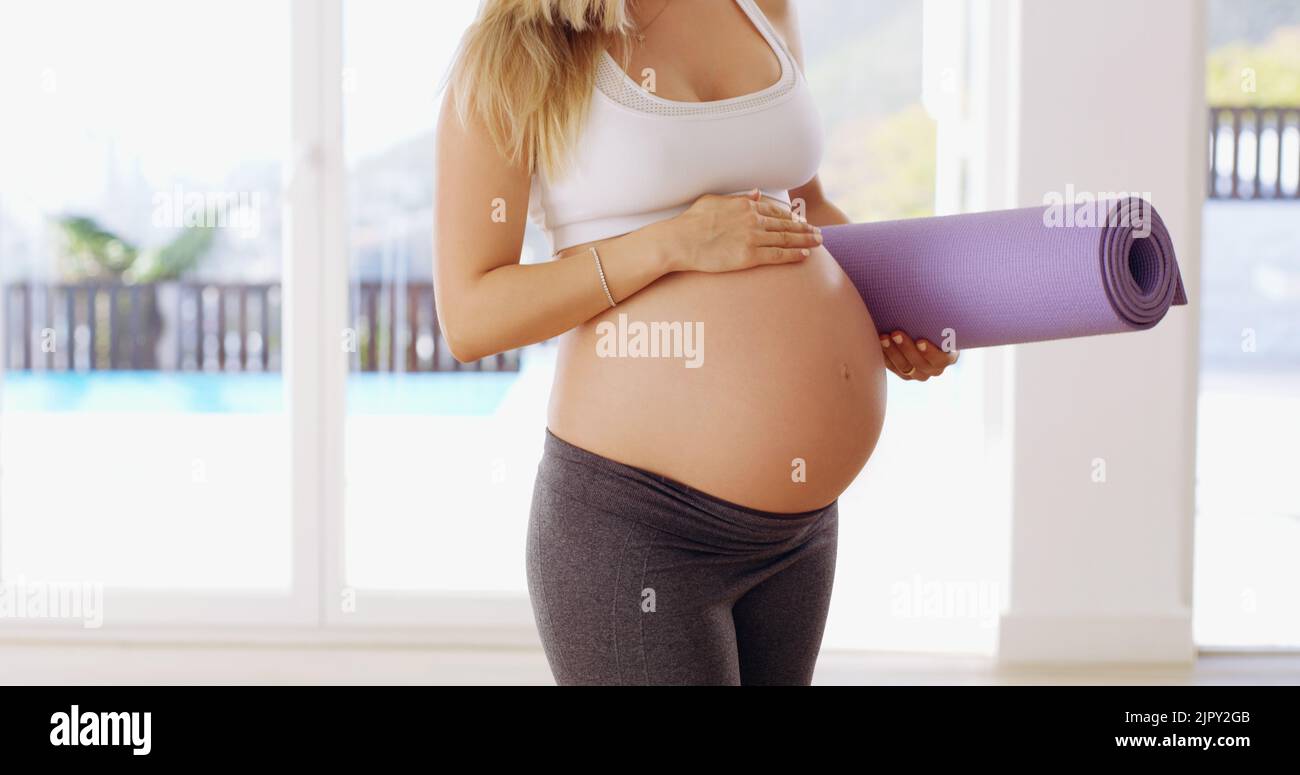 Thats abbastanza il bambino bump. Una giovane donna incinta non riconoscibile che trasporta un tappeto di yoga. Foto Stock