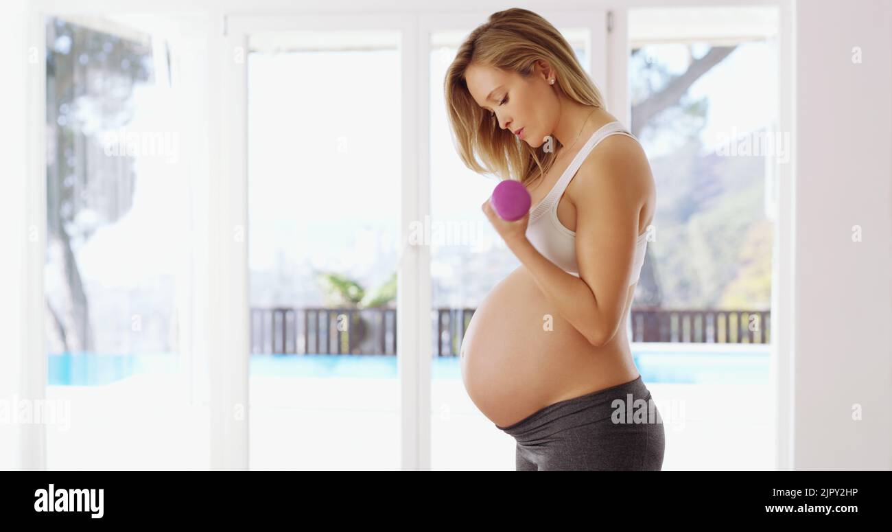 Costruendo la sua forza per il bambino. Una giovane donna incinta attraente che lavora fuori con i dumbbells. Foto Stock
