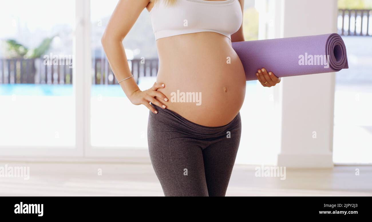 Fiero del suo piccolo bump. Una giovane donna incinta irriconoscibile che porta un tappetino yoga. Foto Stock