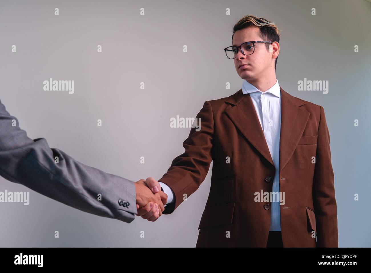 Uomo d'affari che chiude un affare con un'altra persona. Due uomini eleganti che scuotono le mani. Uomo in tuta con giacca marrone, camicia bianca e bicchieri. Due uomini d'affari che tengono la mano. Foto di alta qualità Foto Stock