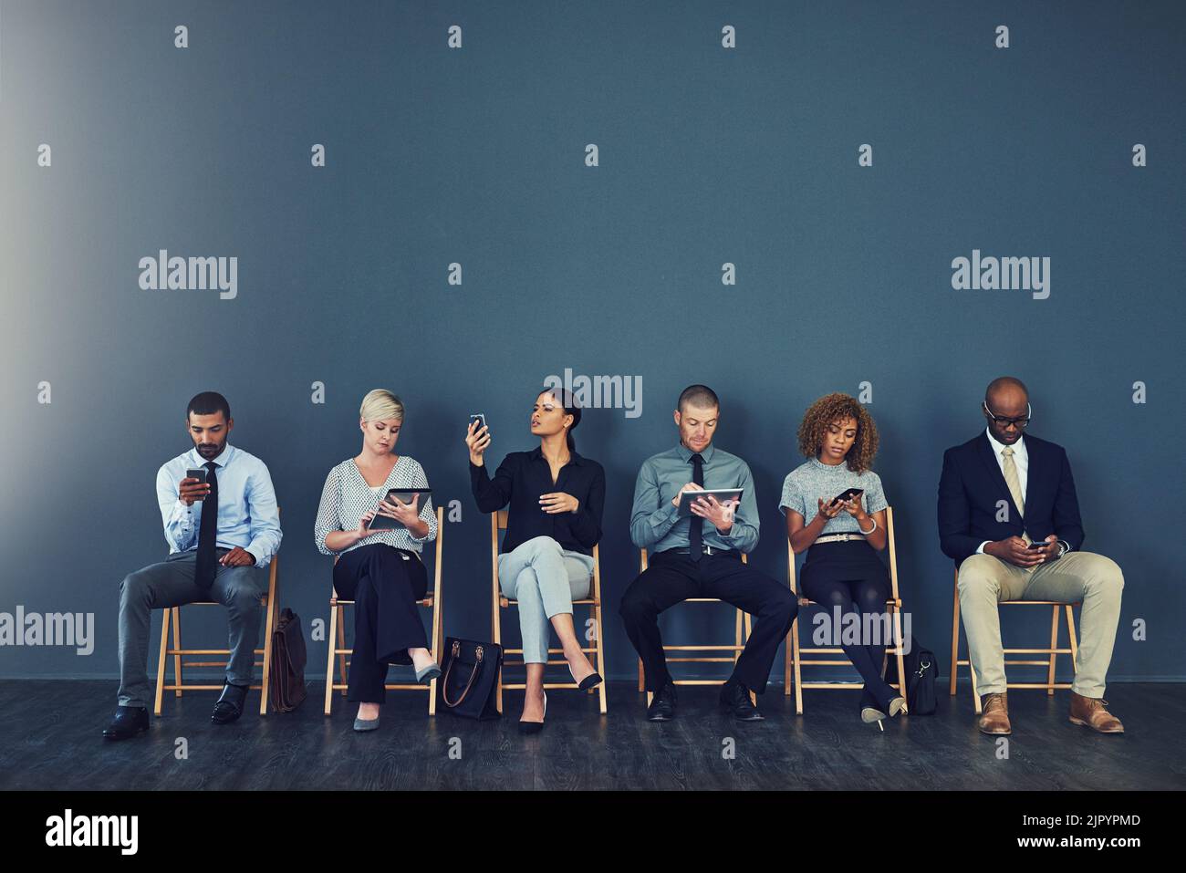 Ora arriva l'attesa. Studio di un gruppo di uomini d'affari che utilizzano dispositivi wireless mentre sono in attesa in linea. Foto Stock