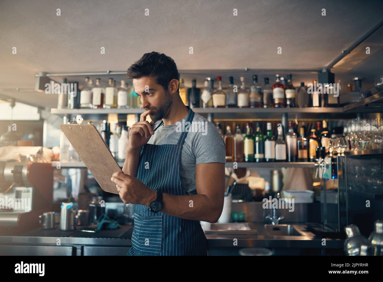 Sembra che Ill abbia a ordinare di più di questo. Un giovane uomo che usa una clipboard mentre lavora dietro un bancone bar. Foto Stock