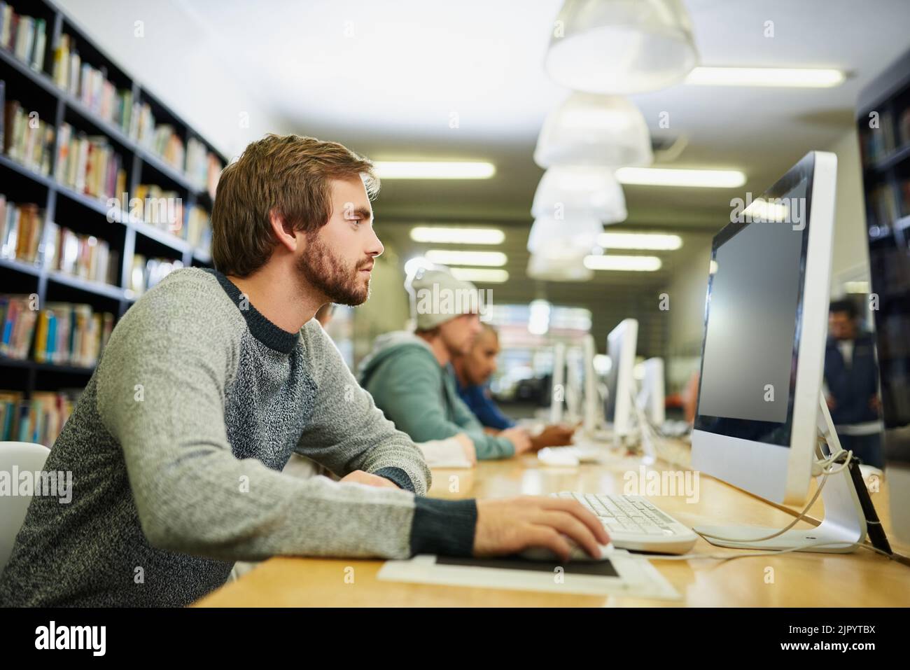 Tutti studiano durante la stagione degli esami, un giovane studente universitario maschile che studia in biblioteca. Foto Stock