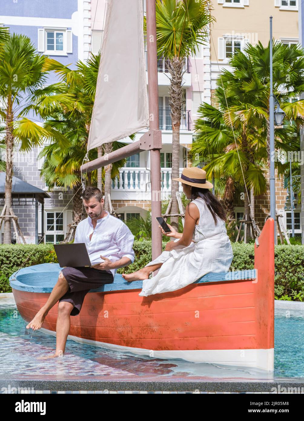 Un paio di uomini e donne con cappelli controllano la valuta crittografica sui loro telefoni quando sono in vacanza. Nomadi digitali che lavorano su computer portatili e telefono Foto Stock