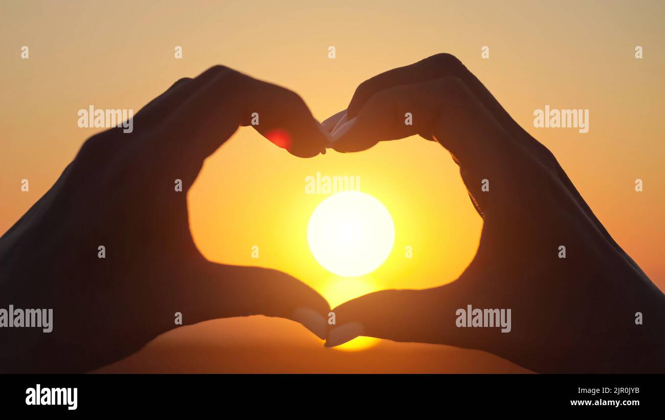 La donna fa il cuore grande con le mani alla parte posteriore del closeup del tramonto Foto Stock