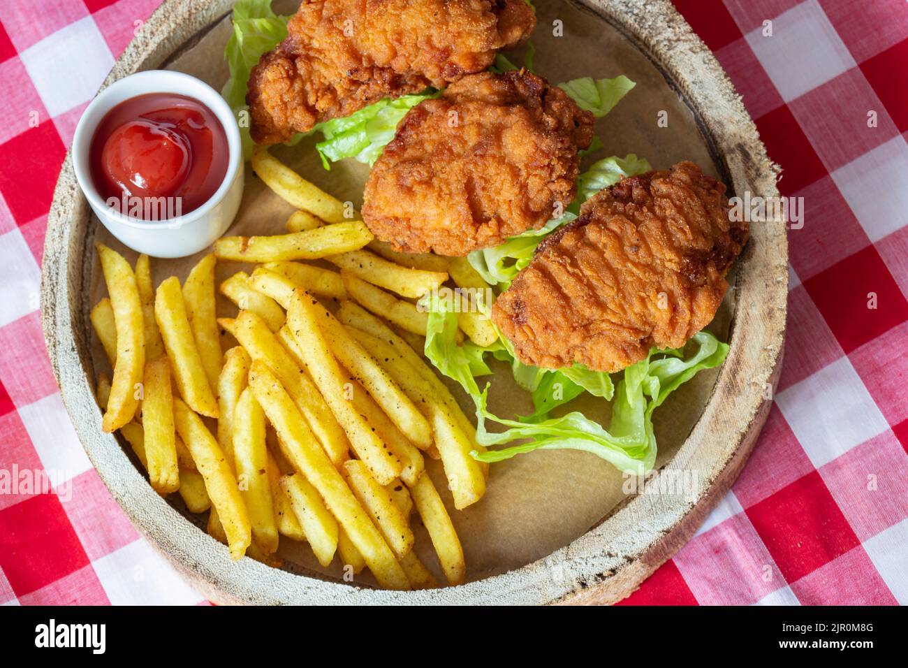 Ali di pollo piccanti, con lattuga patinata e ketchup, su un piatto rustico in legno. Su una tovaglia di Gingham Foto Stock
