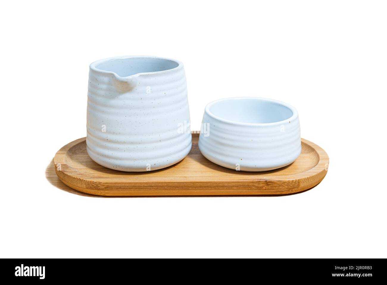 Una tazza di ceramica e una brocca di tè, in argilla bianca, su un piatto di legno su sfondo bianco. Foto Stock