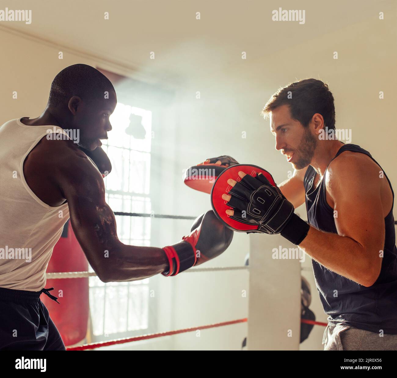 Boxer pratica perforazioni di punzone di uppercut con un personal trainer. Giovane pugile maschio che lancia pugni sui focus pad durante una sessione di allenamento con il suo coa Foto Stock