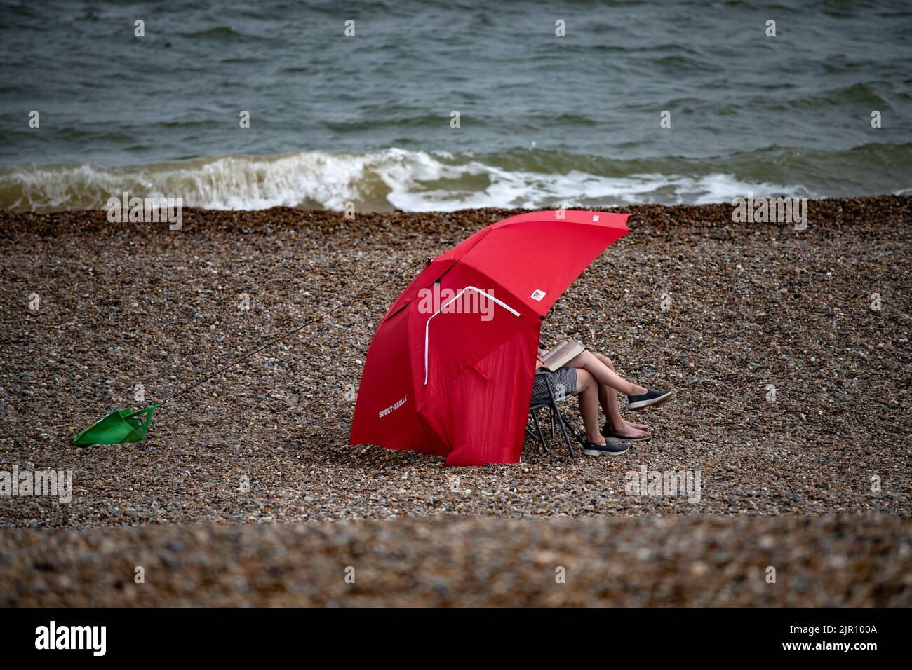Dunwich Beach Suffolk Inghilterra Agosto 2022 al riparo sotto un ombrello sulla spiaggia Foto Stock