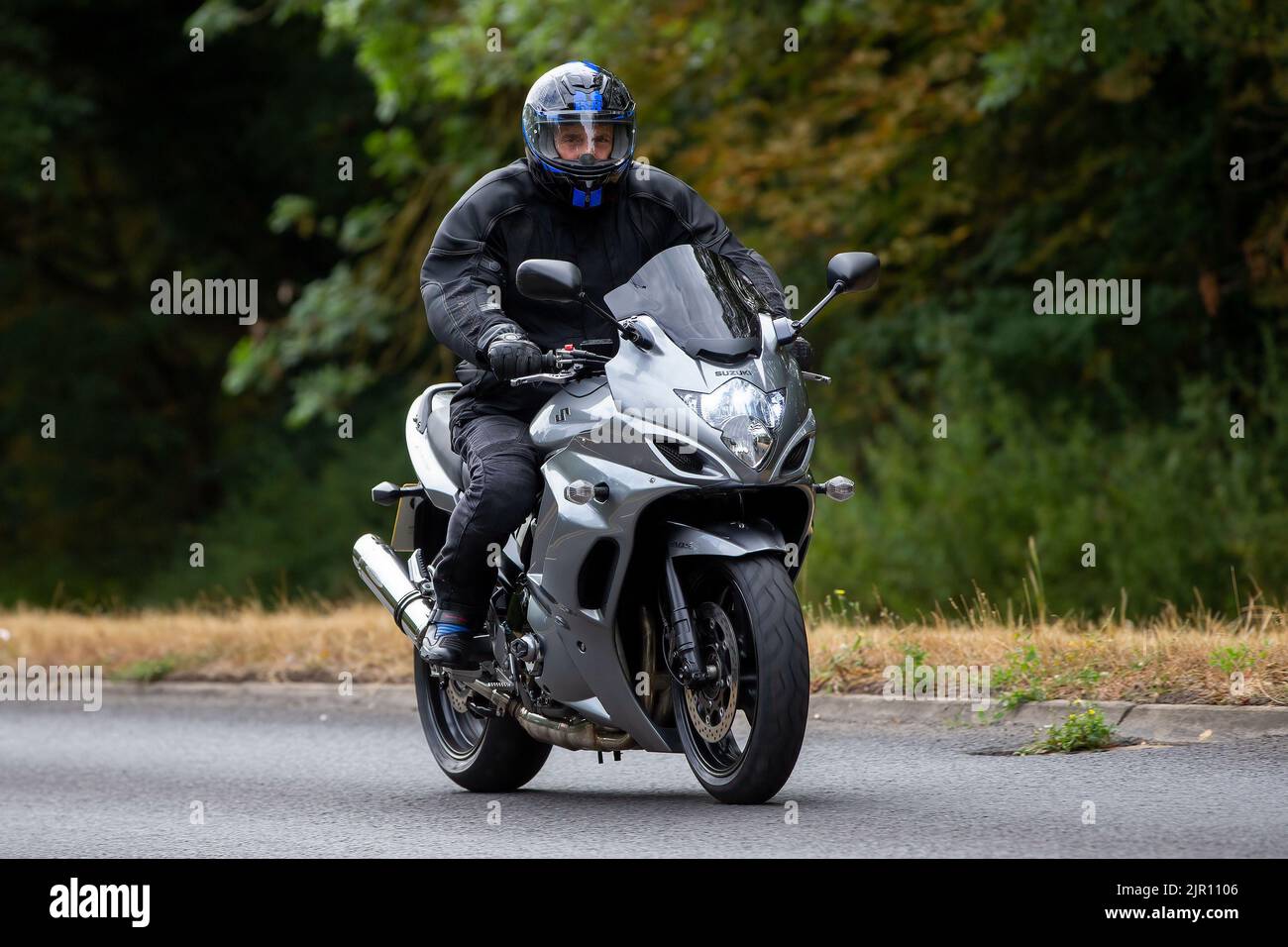 Uomo in nero in sella a una moto Suzuki argentata Foto Stock