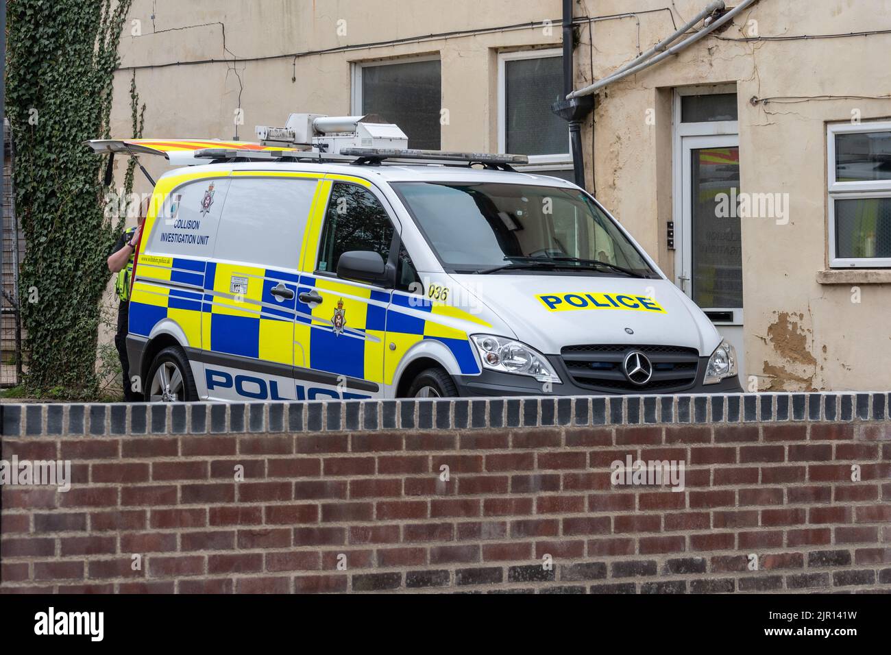 Un furgone della polizia di Wiltshire per le indagini sulle collisioni parcheggiato in una piccola area di parcheggio accanto a un edificio con un ufficiale che lavora sul retro con il boo Foto Stock