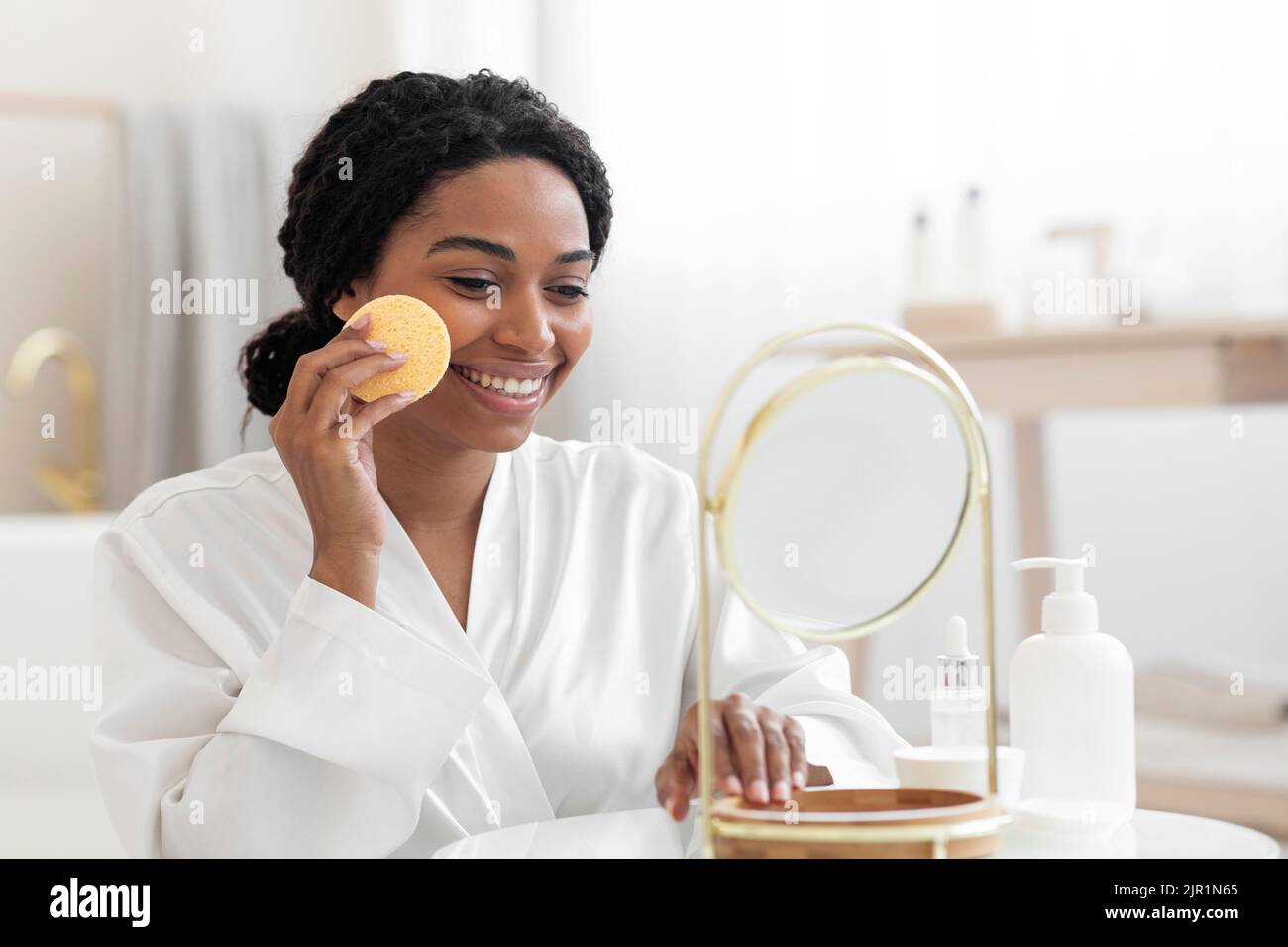 Routine di bellezza. Pelle sorridente nera per la pulizia femminile con spugna cosmetica a casa Foto Stock