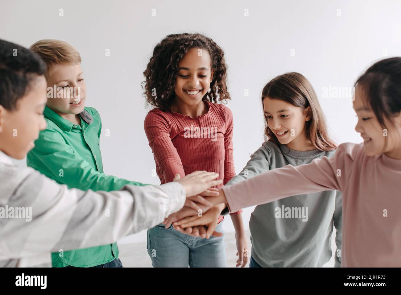 Bambini allegri mettendo le mani insieme in piedi in cerchio in posa al coperto Foto Stock