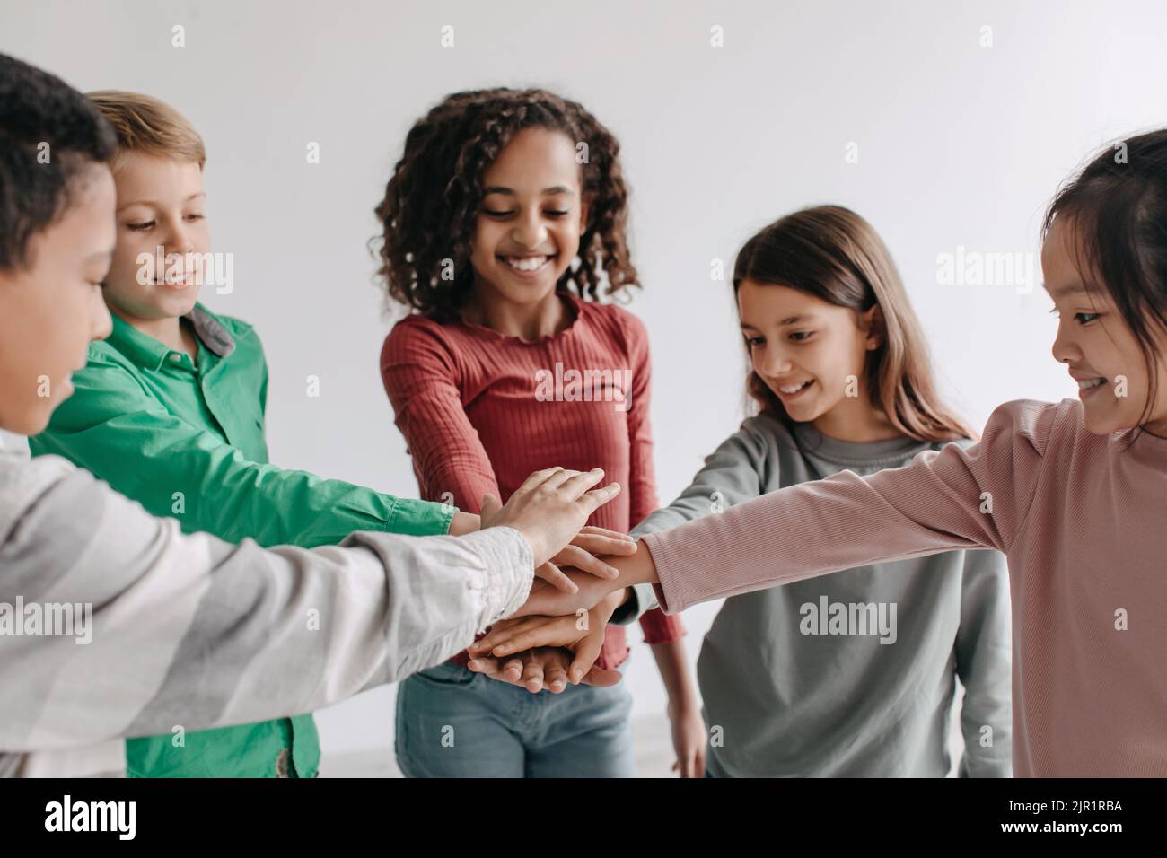Bambini allegri che mettono le mani insieme che posano in piedi all'interno Foto Stock