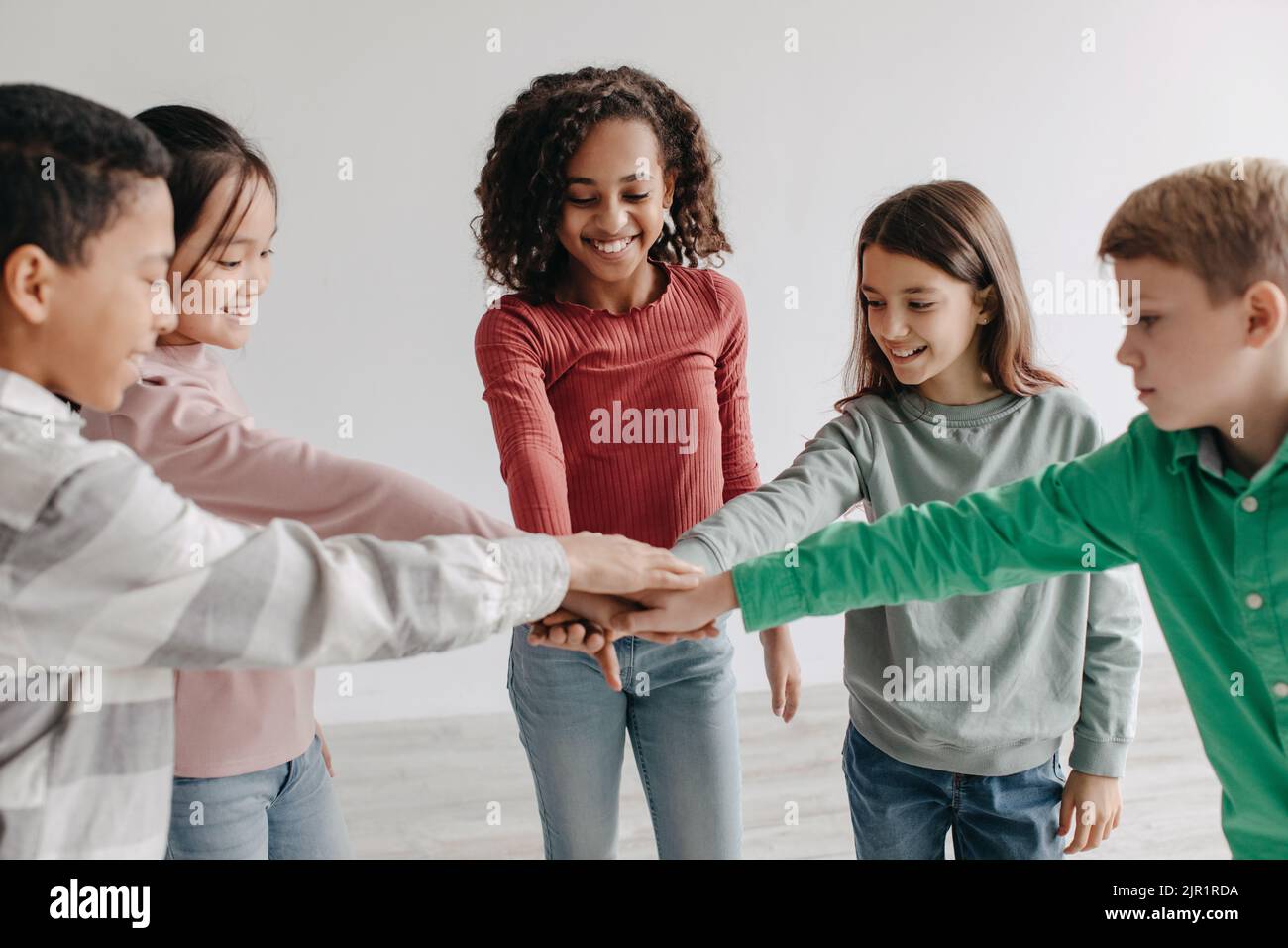 Happy Preteen bambini impilare le mani insieme in piedi in cerchio al chiuso Foto Stock