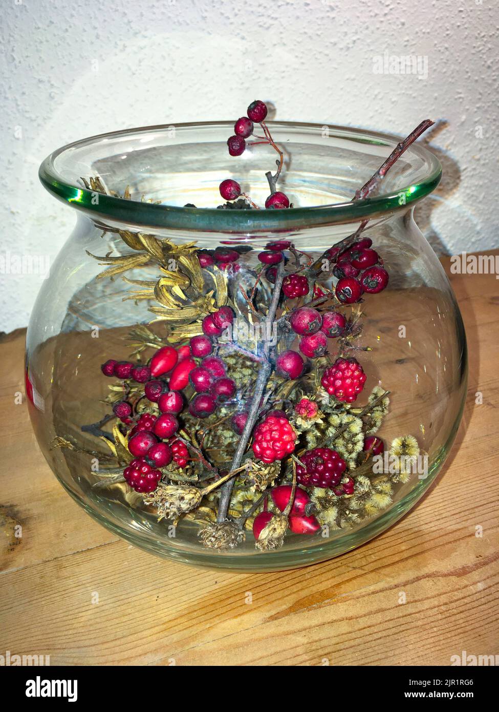 Brombeeren, Ilex, Hagebutte und Gräser in einer Glasvase herbstlich dekoriert Foto Stock