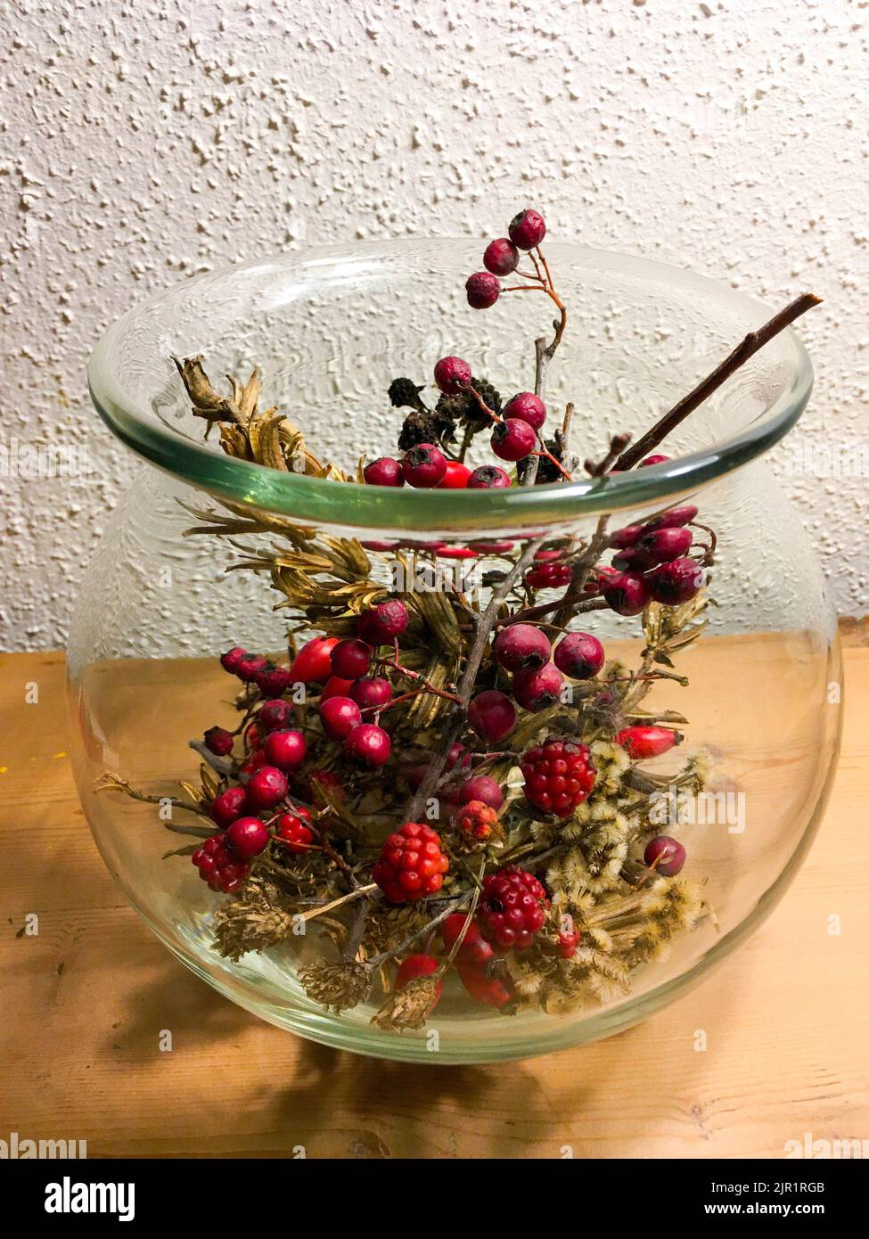 Brombeeren, Ilex, Hagebutte und Gräser in einer Glasvase herbstlich dekoriert Foto Stock