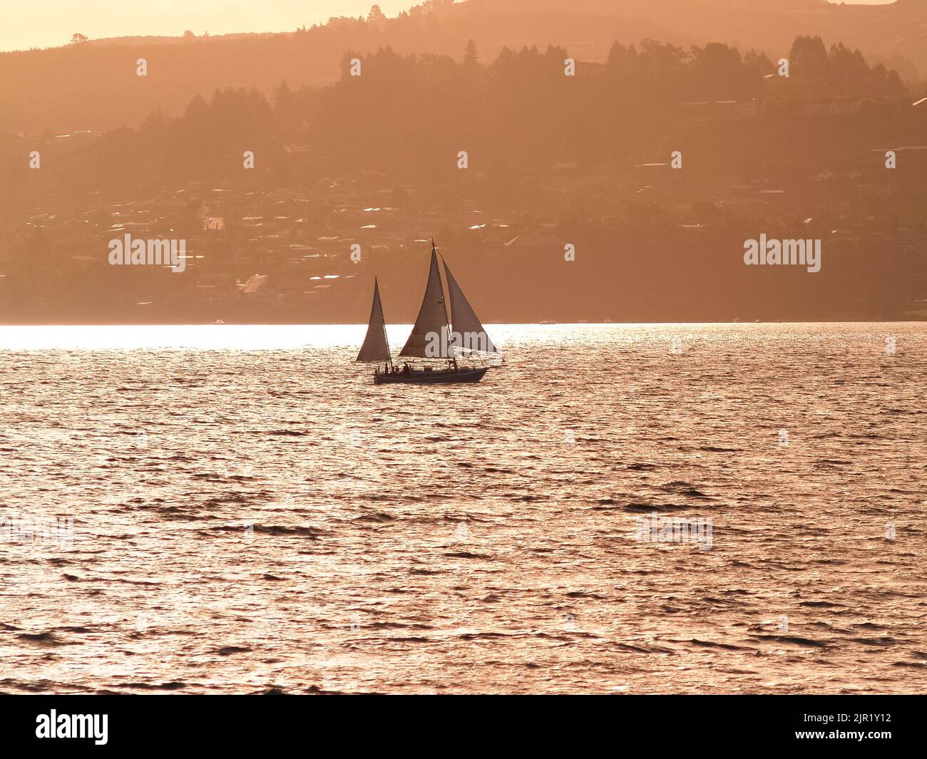 Silhouette colline lontane e yacht in barca a vela sotto il cielo rosso al tramonto sul Lago Taupo, Nuova Zelanda. Foto Stock