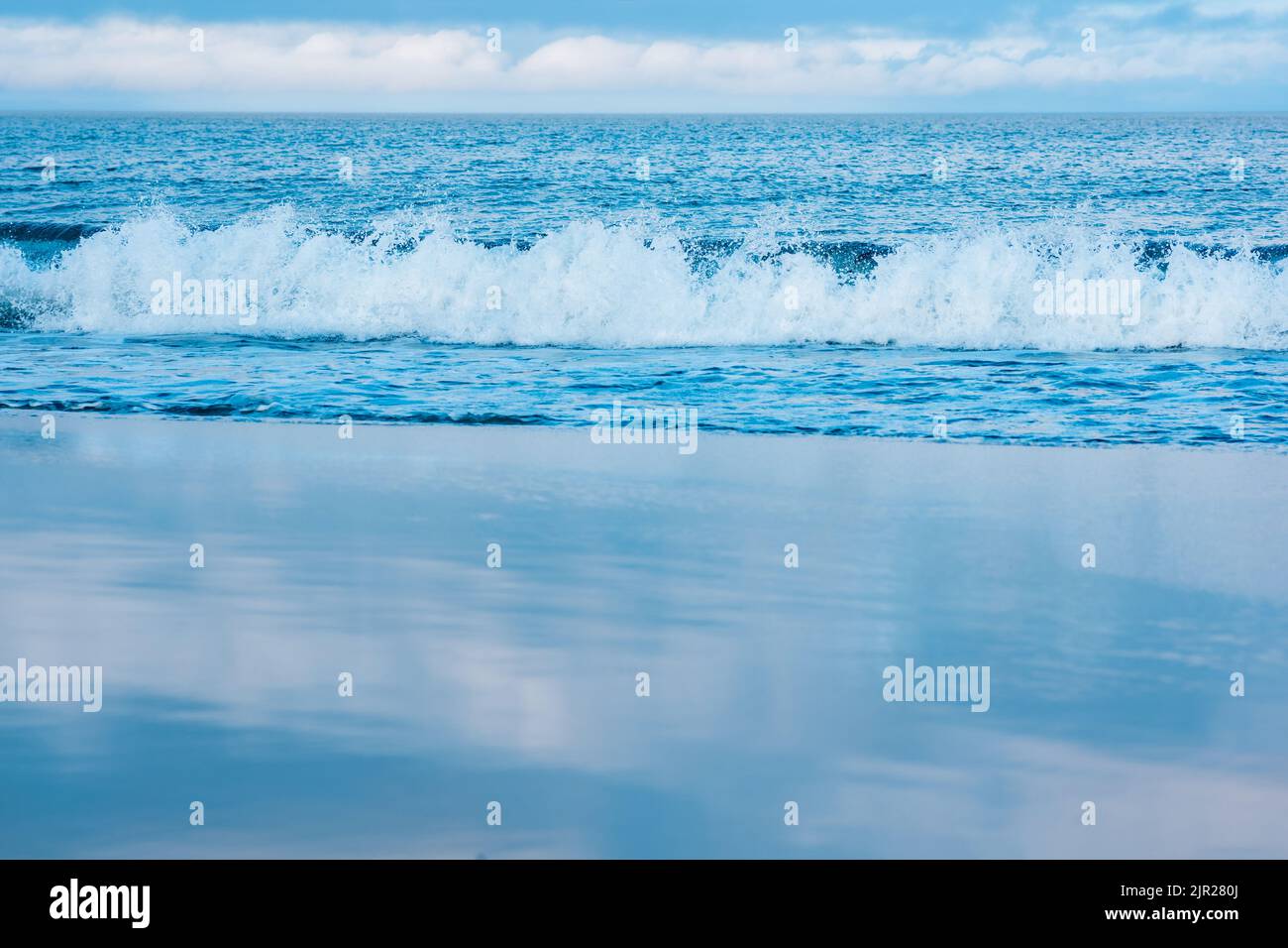 mare, mare surf su una spiaggia di sabbia liscia, il cielo si riflette nella sabbia bagnata Foto Stock