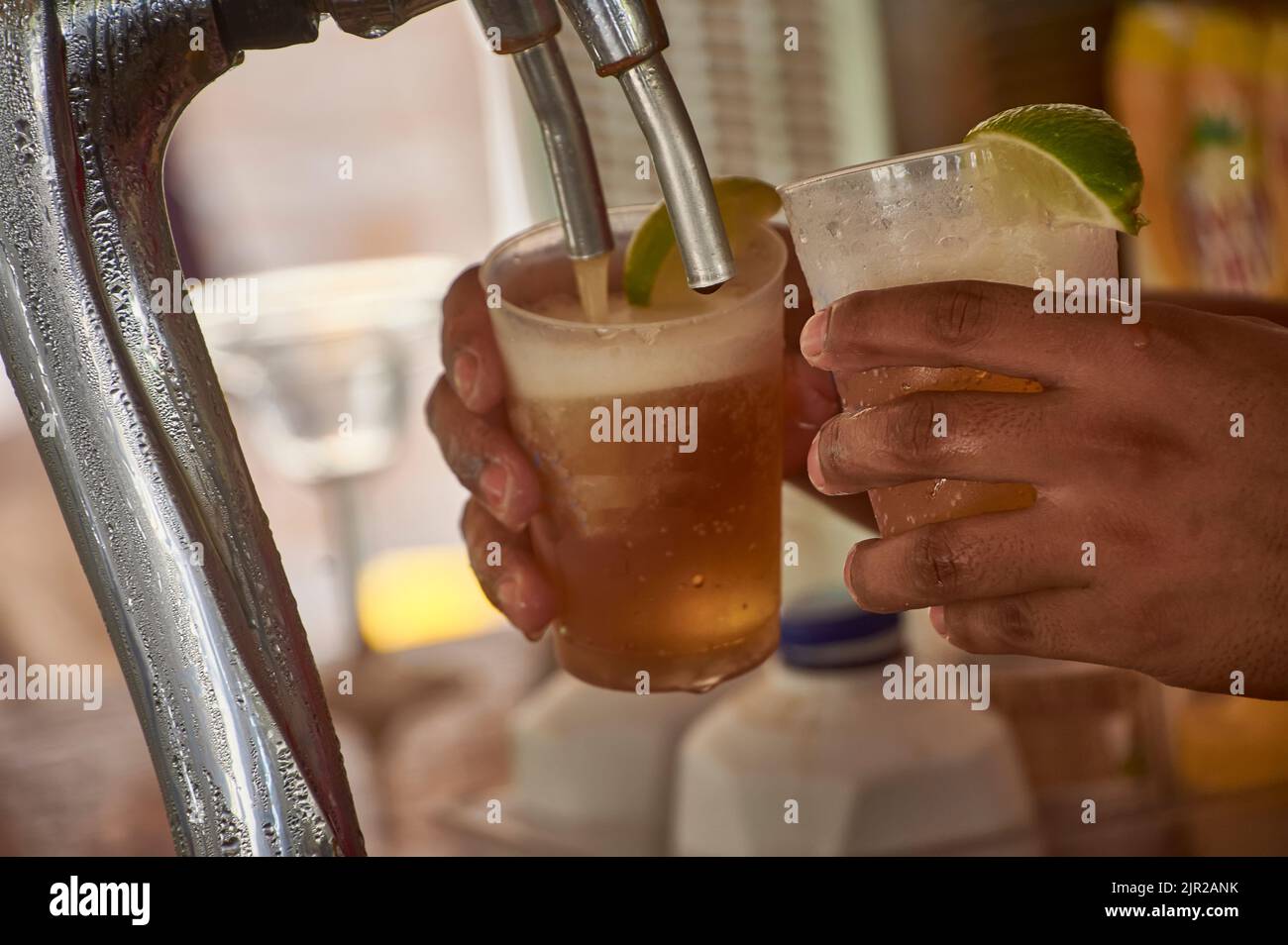 Due bicchieri di birra sotto la spina mentre vengono spinti dalle mani del barman. Foto Stock