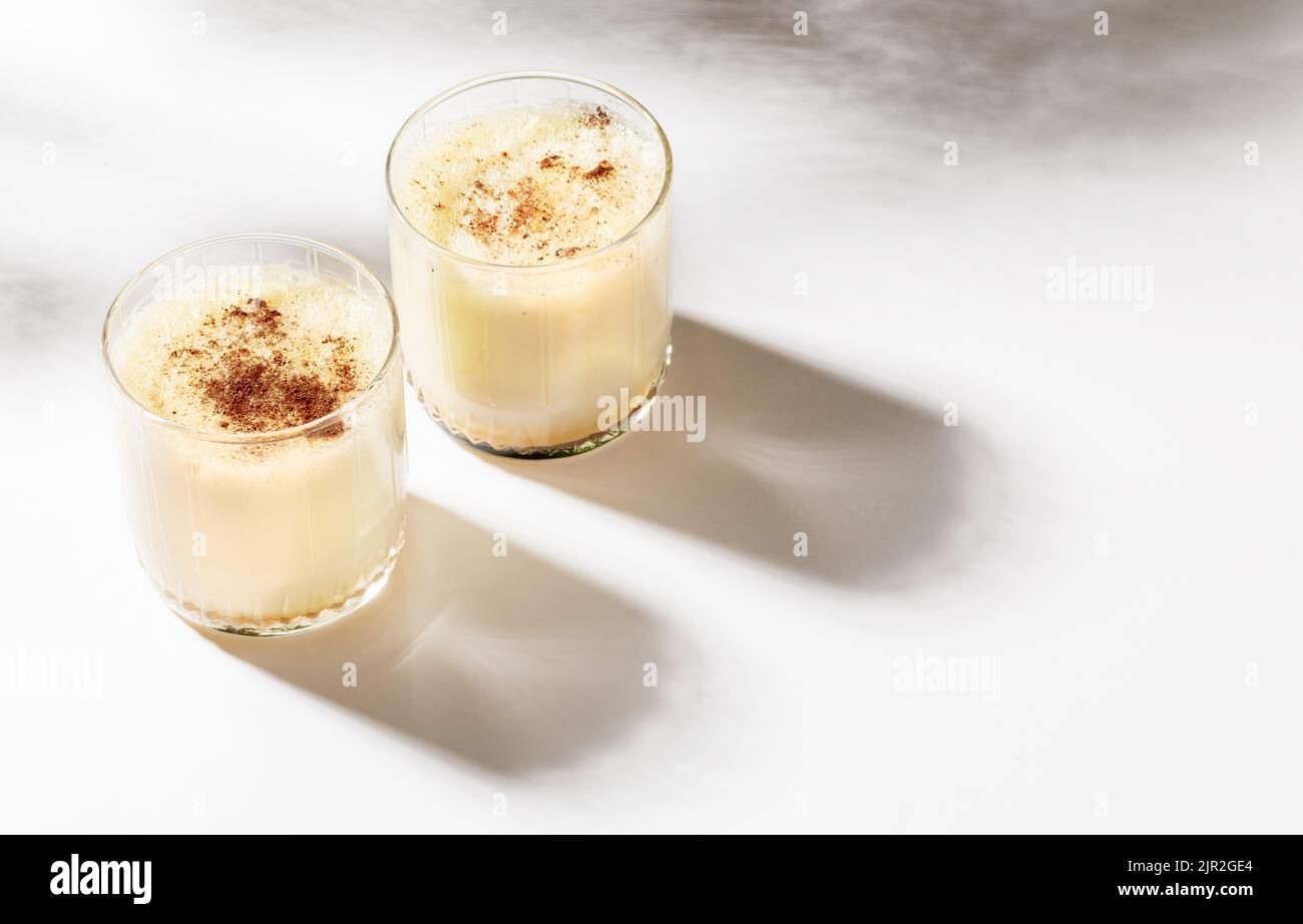 Natale immagine minima con bevanda tradizionale. Due bicchieri con gnog fatto in casa con cannella su sfondo bianco con belle ombre. Selezione f Foto Stock