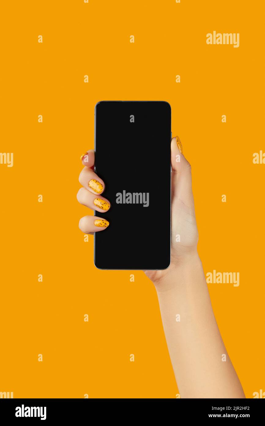 Donna ben curata che tiene lo smartphone nero con schermo vuoto su sfondo arancione Foto Stock