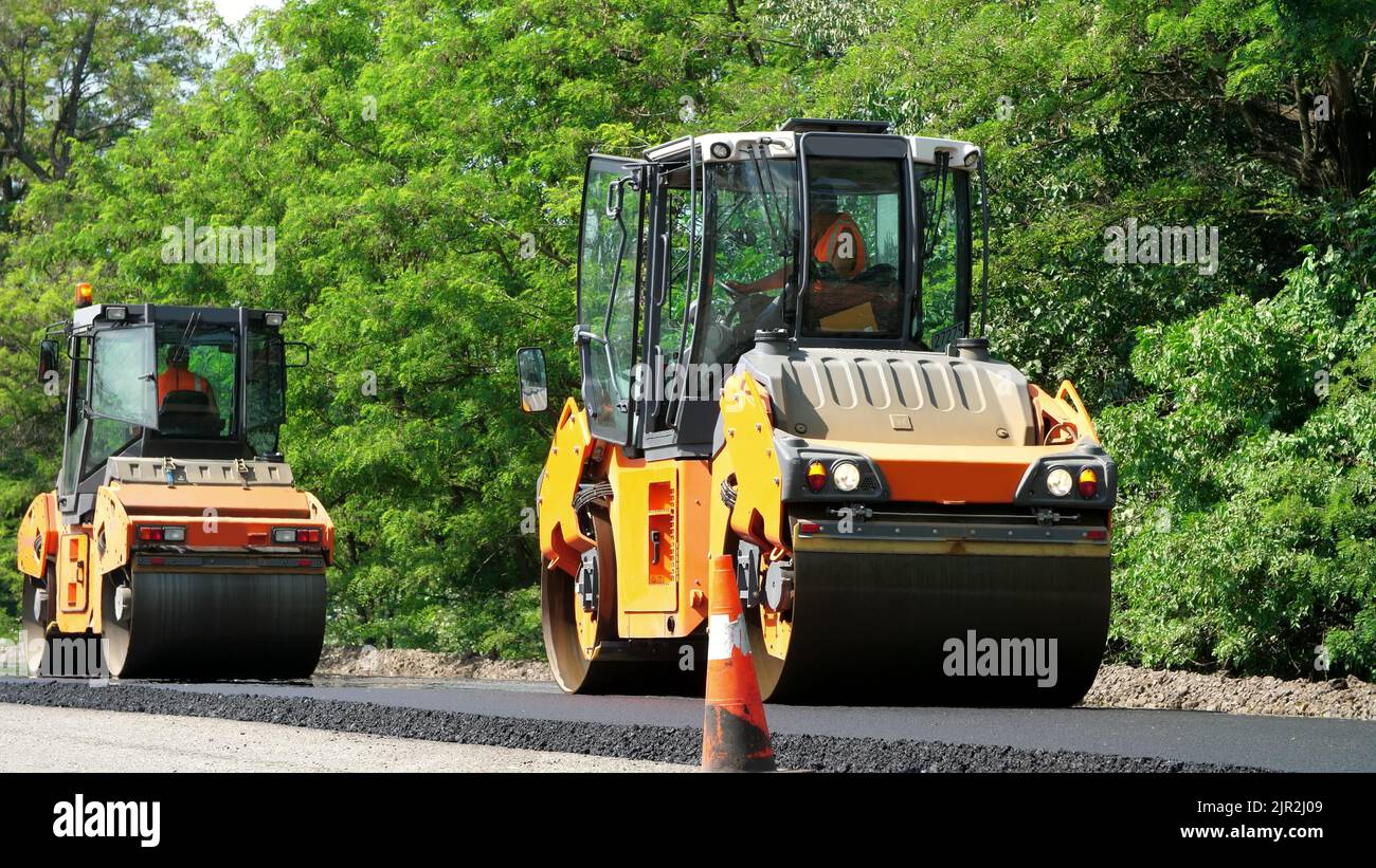 Riparazione di un'autostrada, lavori di costruzione stradale. Compattatore a rulli e finitrice per asfalto posa di una nuova pavimentazione asfaltata fresca,. Foto di alta qualità Foto Stock