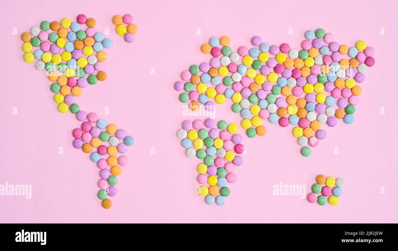 Mappa del mondo fatta con caramelle colorate su bakcgorund rosa pastello. Giacitura piatta. Concetto Terra Foto Stock
