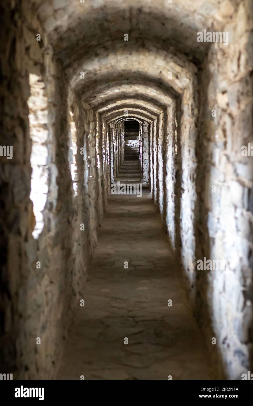 Un lungo corridoio a tunnel in pietra con finestre in un antico castello. Messa a fuoco selettiva. Foto Stock