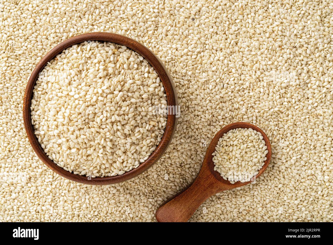 Semi di sesamo crudi in una ciotola di legno e cucchiaio su fondo til bianco. Grani organici di benne per cibo sano, dieta di amplificazione immunità, fonte di calcio. Foto Stock