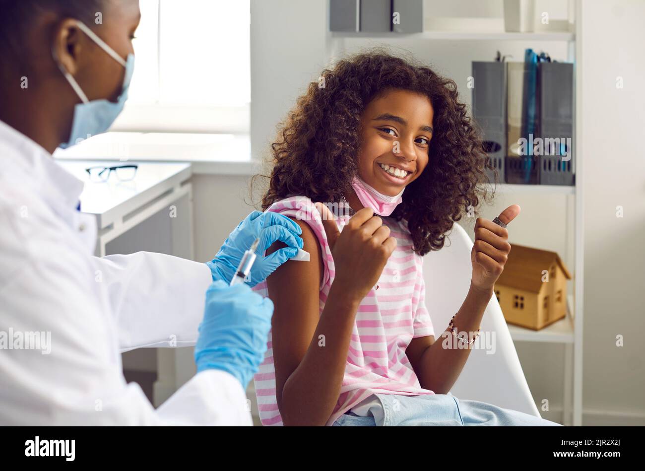 Felice bambino afroamericano riceve l'iniezione del vaccino, sorride e mostra i pollici in su Foto Stock