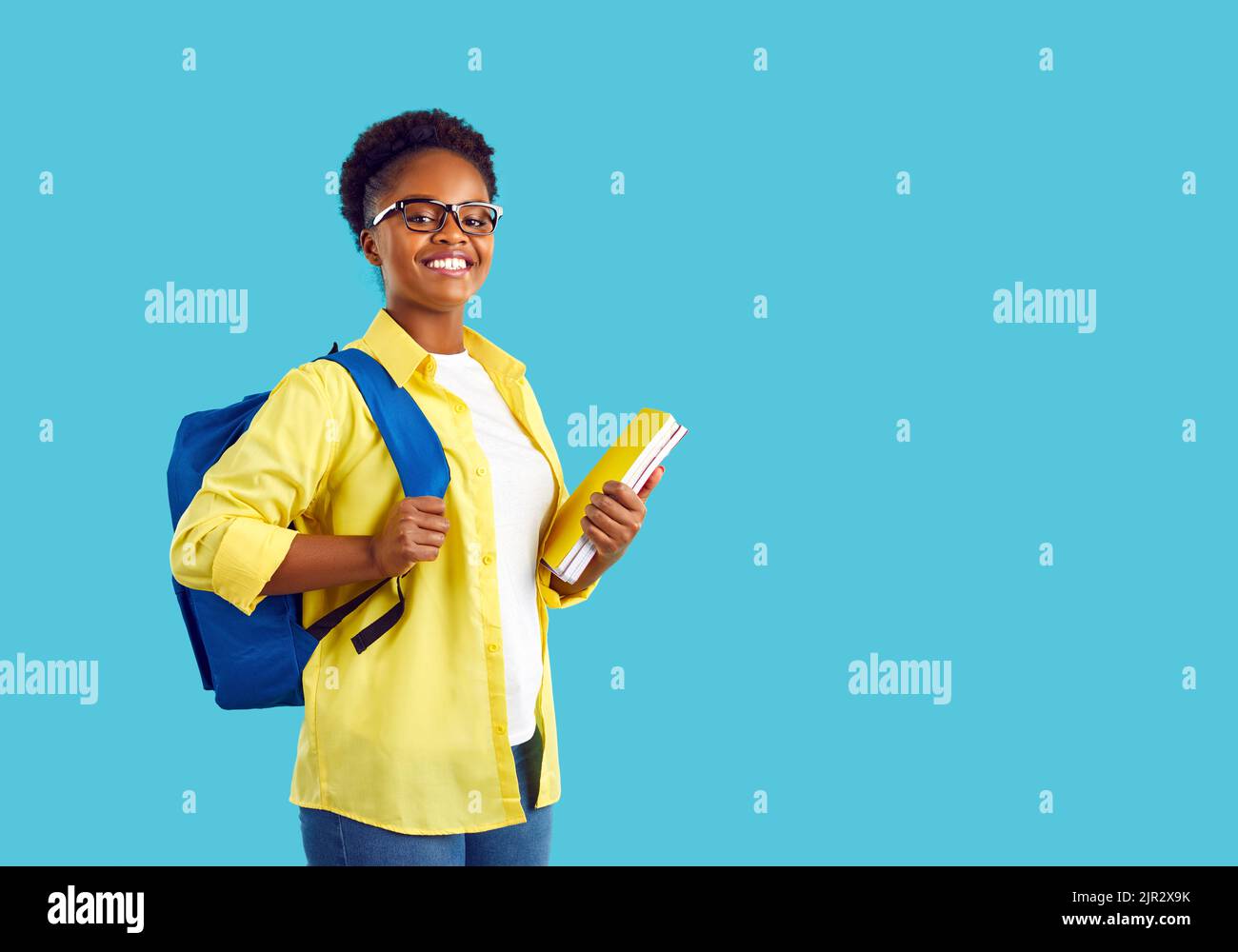Sorridente studentessa internazionale con zaino e libri di testo su sfondo azzurro. Foto Stock