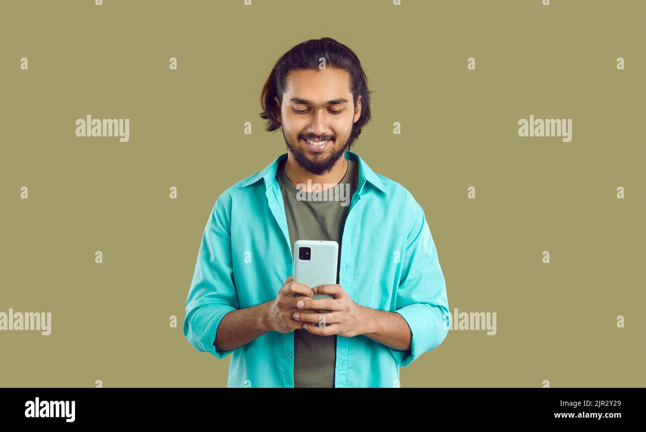 Giovane uomo indiano positivo utilizza moderne applicazioni di telefonia mobile in piedi in studio verde Foto Stock