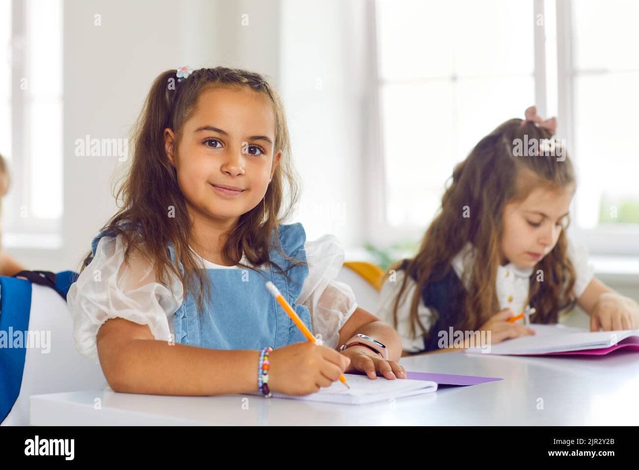 Ritratto di simpatica bambina sorridente seduta in classe e godendosi gli studi. Foto Stock