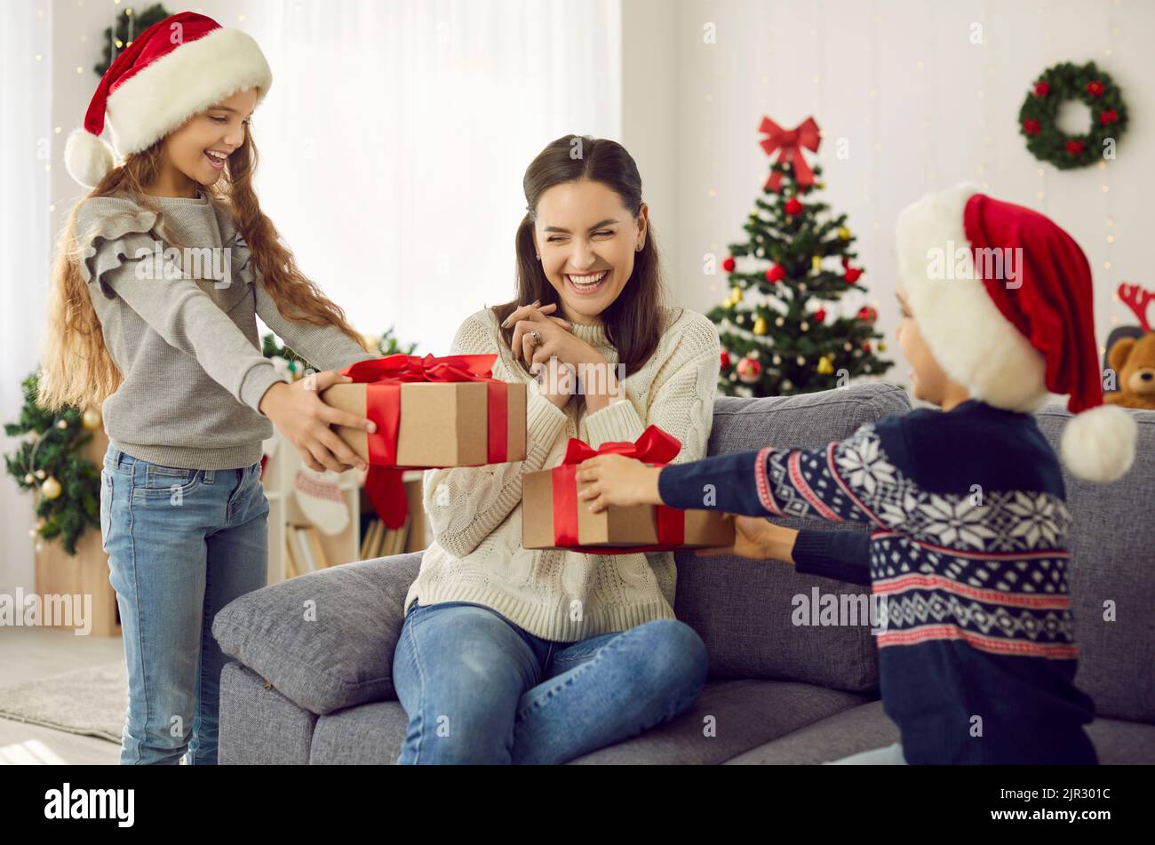 Figliuola e figlio che danno regali alla loro giovane madre felice il giorno di Natale Foto Stock