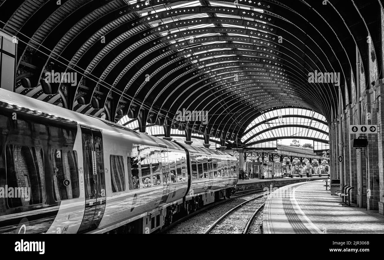 Accanto alla piattaforma della stazione ferroviaria si trova un treno. Ci sono dei passeggeri sullo sfondo e una storica tettoia curva è sopra. Foto Stock